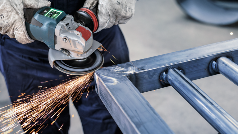 PRO Backing Pad Soft, 125 mm, X-Lock Person wearing safety equipment grinds a metal frame, producing bright sparks.