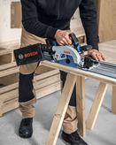 A person wearing safety equipment cuts wood with a circular saw on a workbench.