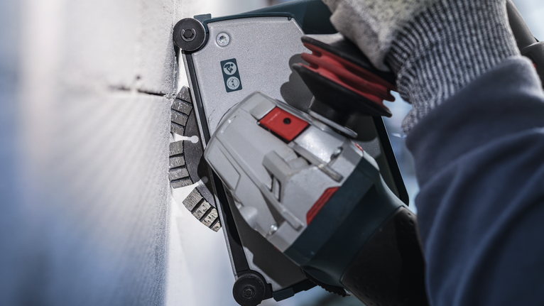 Person wearing safety equipment uses a power tool to cut into a concrete wall.