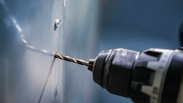 A power drill makes a hole in a metal panel.