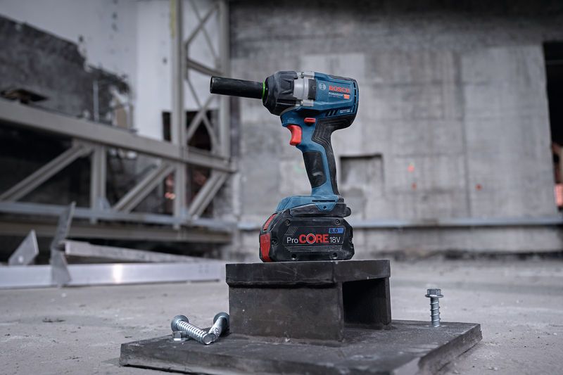 Cordless impact wrench resting on a metal block with two large bolts nearby.