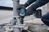 A person wearing safety equipment tightens a large bolt on a metal structure with a cordless impact wrench.
