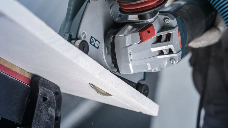 PRO Marble Diamond Disc, 115 x 22.23 mm Person wearing safety equipment cuts a tile with a handheld power cutter.