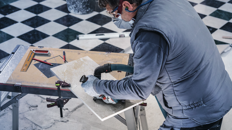 PRO Marble Diamond Disc, 115 x 22.23 mm Person wearing safety equipment cuts a tile with a power tool on a workbench.