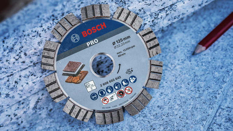 Segmented diamond cutting disc placed on a granite tile near a red carpenter pencil.