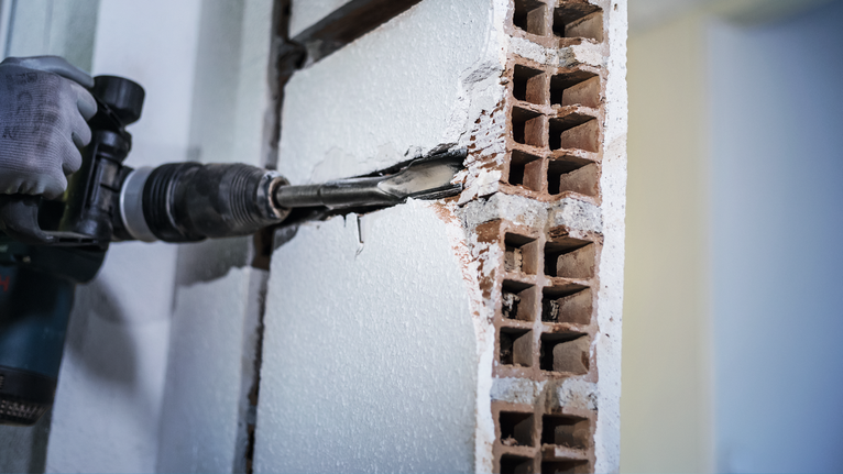 PRO SDS max Hollow Gouging Chisel, 32 x 300 mm A person wearing safety equipment uses a rotary hammer to chip away a brick wall.
