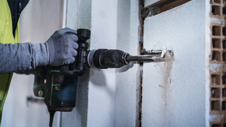 PRO SDS max Hollow Gouging Chisel, 32 x 300 mm A person wearing safety equipment uses a power drill to bore a hole in a wall.