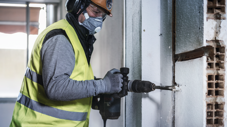 PRO SDS max Hollow Gouging Chisel, 32 x 300 mm A person wearing safety equipment drills into a concrete wall.