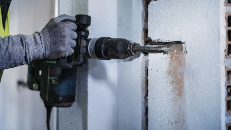 PRO SDS max Hollow Gouging Chisel, 32 x 300 mm A person wearing safety equipment uses a rotary hammer to chisel a rectangular slot in a wall.