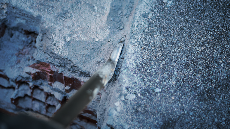 PRO HEX 30-4C Spade Chisel, 75 x 450 mm Pointed chisel breaking through concrete along a rough wall edge.