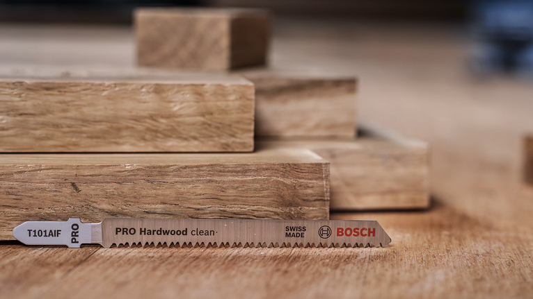 PRO Hardwood clean T101AIF Jigsaw Blade, 100 mm, 5 pcs A saw blade lies on a wooden surface beside stacked wooden planks.