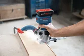 A person uses a cordless router to shape the edge of a wooden board.