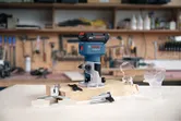 Cordless trim router and attachments displayed on a workbench in a woodworking shop.