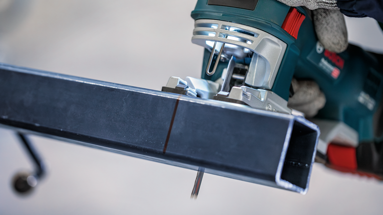 Person wearing safety equipment uses a jigsaw to cut a metal beam.