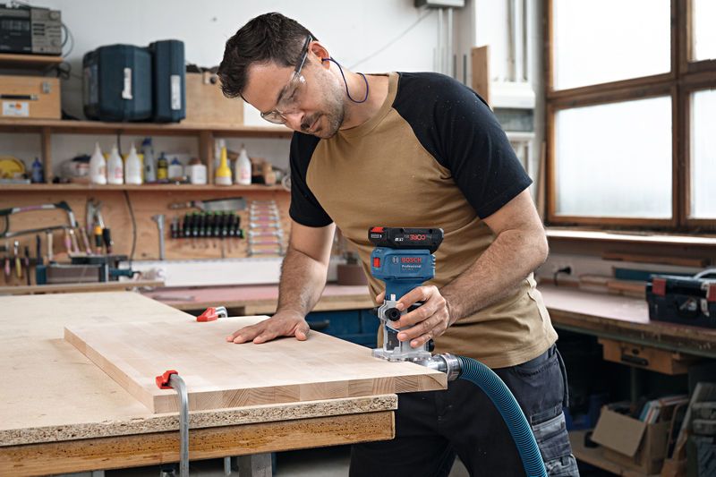 GLF 18V-8 Person wearing safety equipment uses a wood router on a clamped board in a workshop.