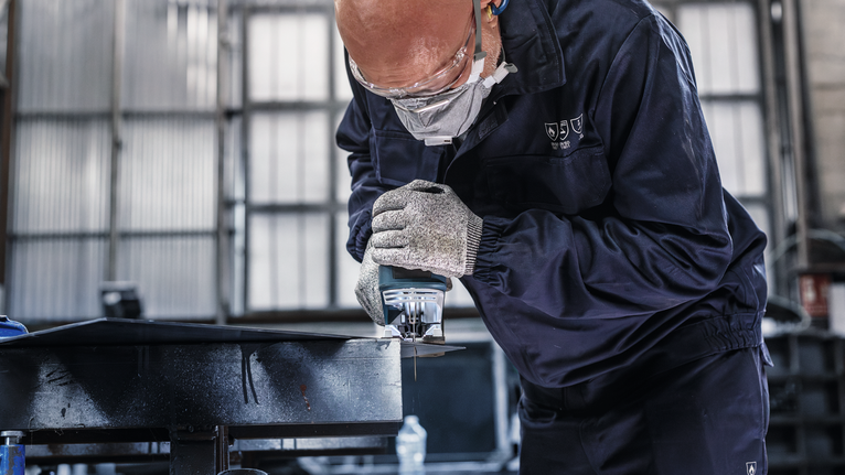 PRO Metal thick and thin T123XF Jigsaw Blade, 100 mm, 5 pcs Person wearing safety equipment cuts metal using a handheld power saw.