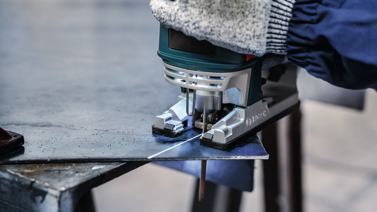 PRO Metal thick and thin T123XF Jigsaw Blade, 100 mm, 5 pcs A person wearing safety equipment cuts a sheet of metal with a jigsaw.