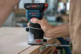 A person uses a cordless palm router to trim the edge of a wooden board.