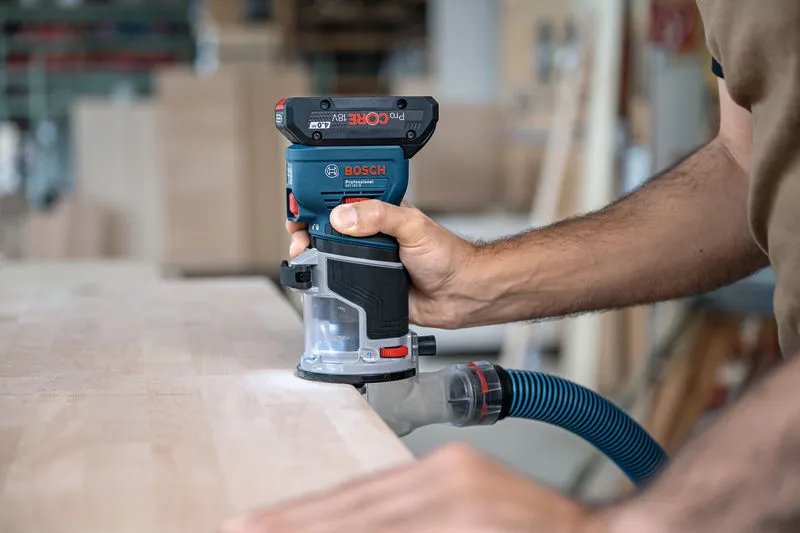 GKF 18V-8 A person guides a cordless palm router along the edge of a wooden board.
