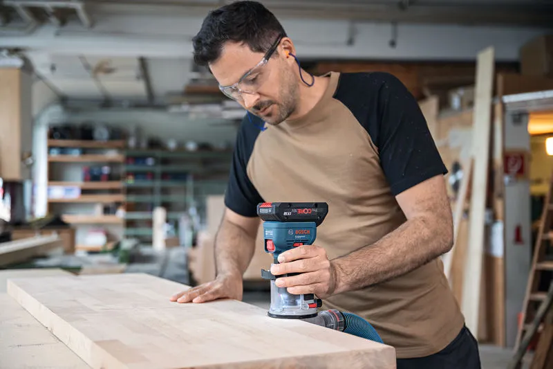 GKF 18V-8 A person wearing safety equipment routes the edge of a wooden board with a cordless palm router.