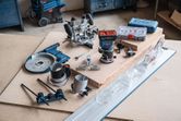Cordless palm router with various woodworking accessories and attachments on a workbench.