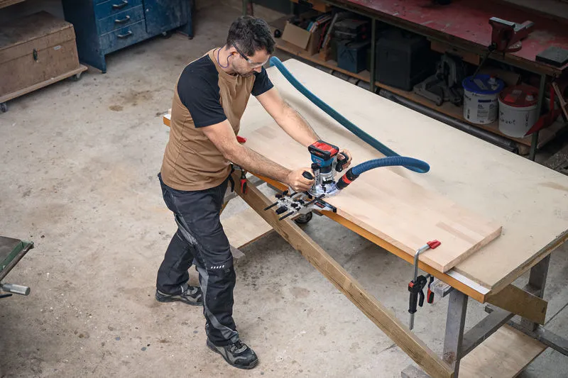 GKF 18V-8 A person wearing safety equipment uses a cordless palm router on a wooden board.