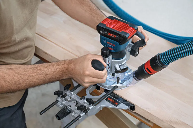 GKF 18V-8 A person uses a cordless palm router with a dust extraction attachment on wood.