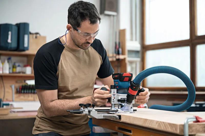 GKF 18V-8 A person wearing safety equipment operates a cordless palm router on a wooden board.