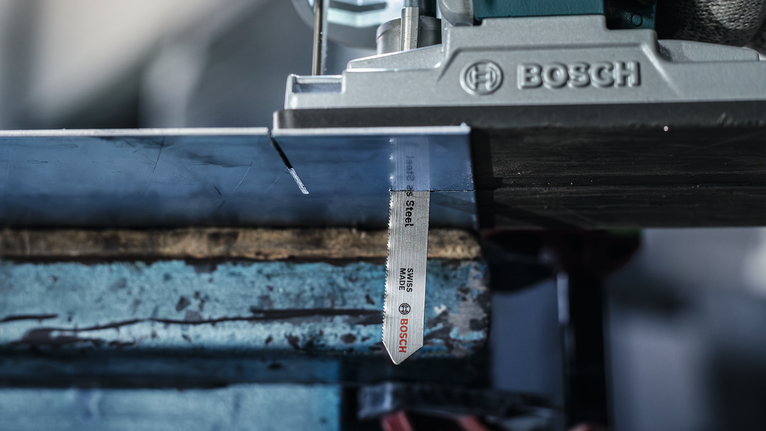 Jigsaw blade cutting through a metal sheet clamped to a workbench.