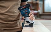 A person operates a cordless palm router on a wooden board.
