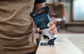 A person operates a cordless palm router on a wooden board.