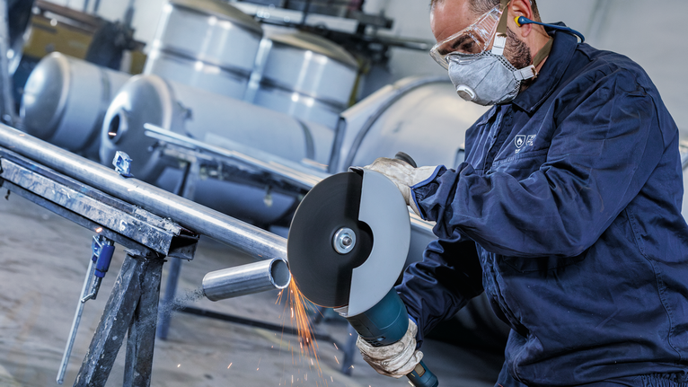 PRO Stainless Steel and Metal Bonded Cutting Disc, 180 x 1.6 x 22.23 mm, Straight, oSa A person wearing safety equipment cuts a metal pipe with a large angle grinder.