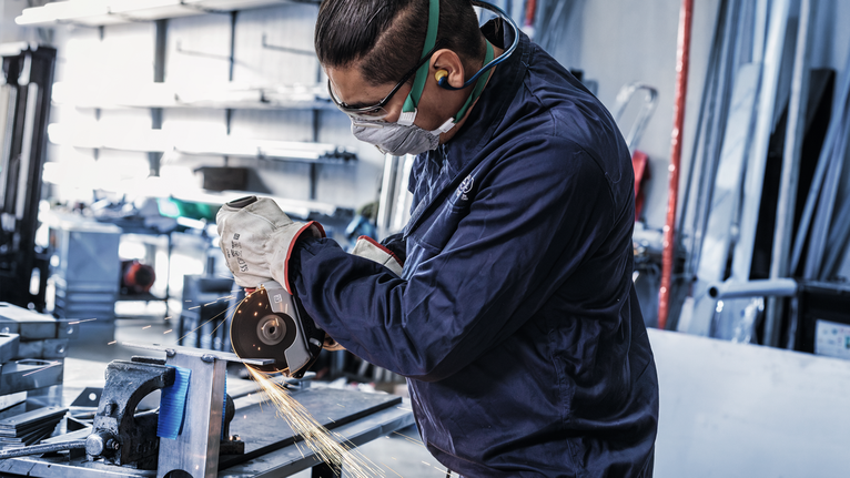 PRO Stainless Steel and Metal Bonded Cutting Disc, 125 x 1.6 x 22.23 mm, X-Lock, Straight, oSa A person wearing safety equipment grinds metal, creating sparks in a workshop.