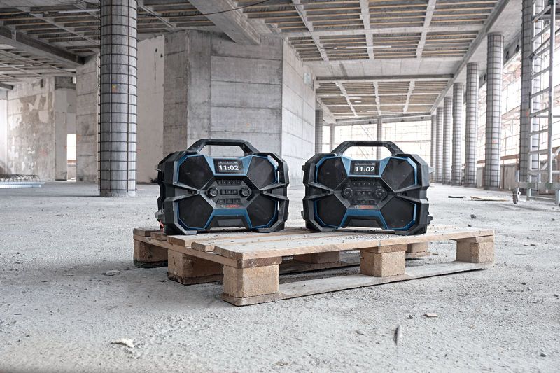 Two rugged construction site radios placed on a wooden pallet in a partially built structure.