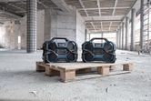 Two rugged construction site radios placed on a wooden pallet in a partially built structure.