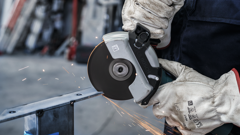 PRO Stainless Steel and Metal Bonded Cutting Disc, 125 x 1.6 x 22.23 mm, X-Lock, Straight, oSa A person wearing safety equipment cuts metal with a circular saw, creating sparks.