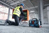 A person wearing safety equipment connects wires at a construction site near a jobsite radio.
