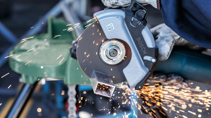 Object #200467094: 3089912_app_web_3 A worker wearing safety equipment cuts a metal pipe with an angle grinder, sparks flying.