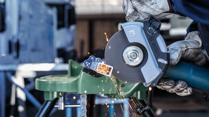 Object #200467096: 3089912_app_web_5 A worker wearing safety equipment uses a cut-off saw to cut a metal bar, producing sparks.
