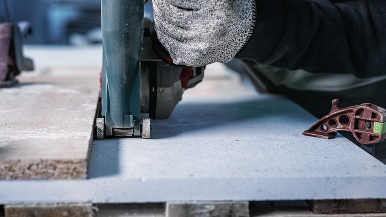 Person wearing safety equipment cutting a concrete slab with a power saw.