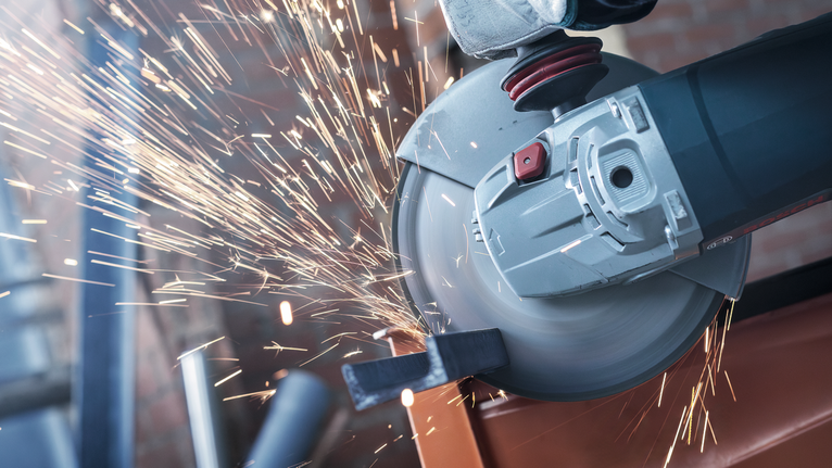 Person wearing safety equipment grinds metal, creating bright sparks.