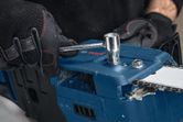 A person wearing safety equipment adjusts a cordless chainsaw with a wrench.