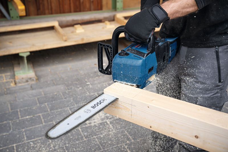 A person wearing safety equipment cuts a wooden beam with a cordless chainsaw.
