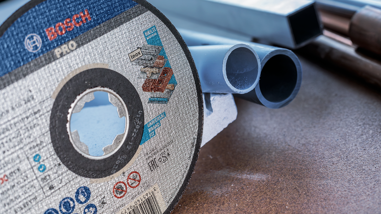 Cutting disc resting on a workbench beside several plastic pipes.