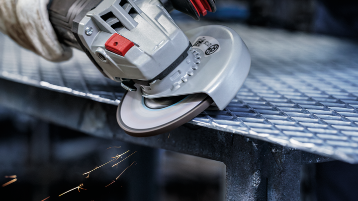 Gloved hand grinds metal grating with an angle grinder, sparks flying.