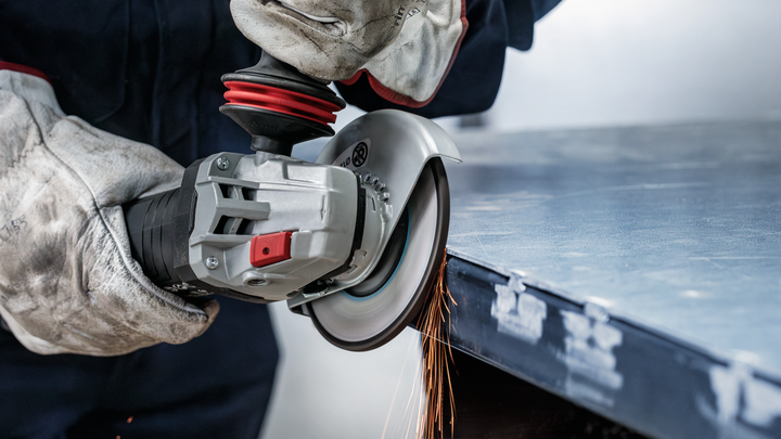 Worker wearing safety equipment grinds metal, producing sparks at the edge of a sheet.