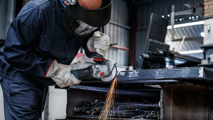 A worker wearing safety equipment grinds metal, creating bright sparks.