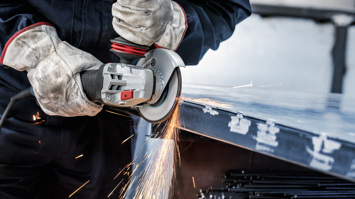 Worker wearing safety equipment grinds metal sheet, producing bright sparks.