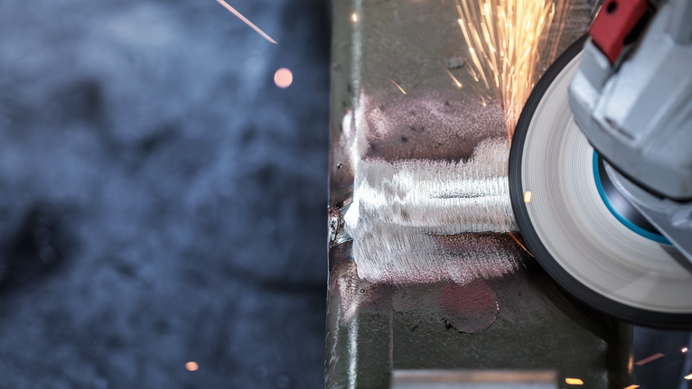 PRO Metal Bonded Grinding Disc, 125 x 6 x 22.23 mm, X-Lock Angle grinder smoothing a metal weld, creating sparks.