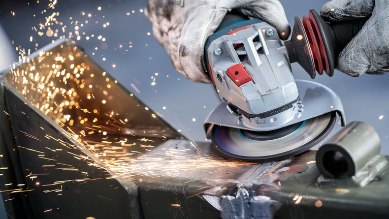 PRO Metal Bonded Grinding Disc, 125 x 6 x 22.23 mm, X-Lock Person wearing safety equipment grinds metal, producing bright sparks.